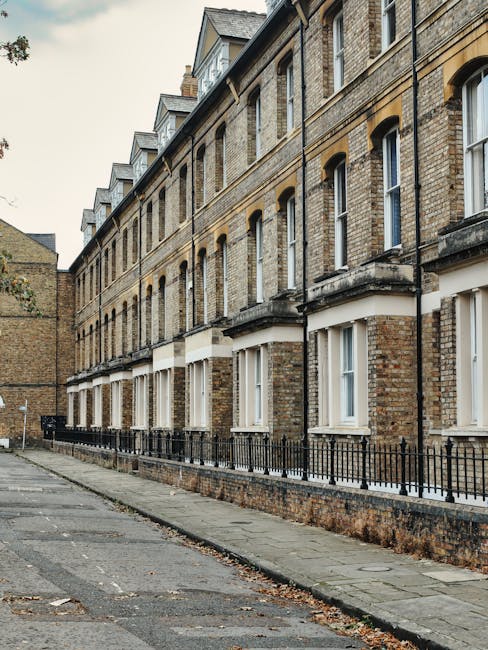 Exterior view of a row of Victorian terraced houses with decorative bay windows and detailed brickwork, painted in various pastel shades including blue, cream, and light green. The buildings feature l
